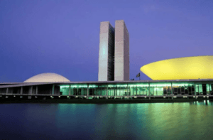 Fachada iluminada do Congresso Nacional, em Brasília, à noite, com destaque para a arquitetura icônica e o reflexo na água. Ideal para ilustrar segurança perimetral de grandes áreas públicas e estratégicas.